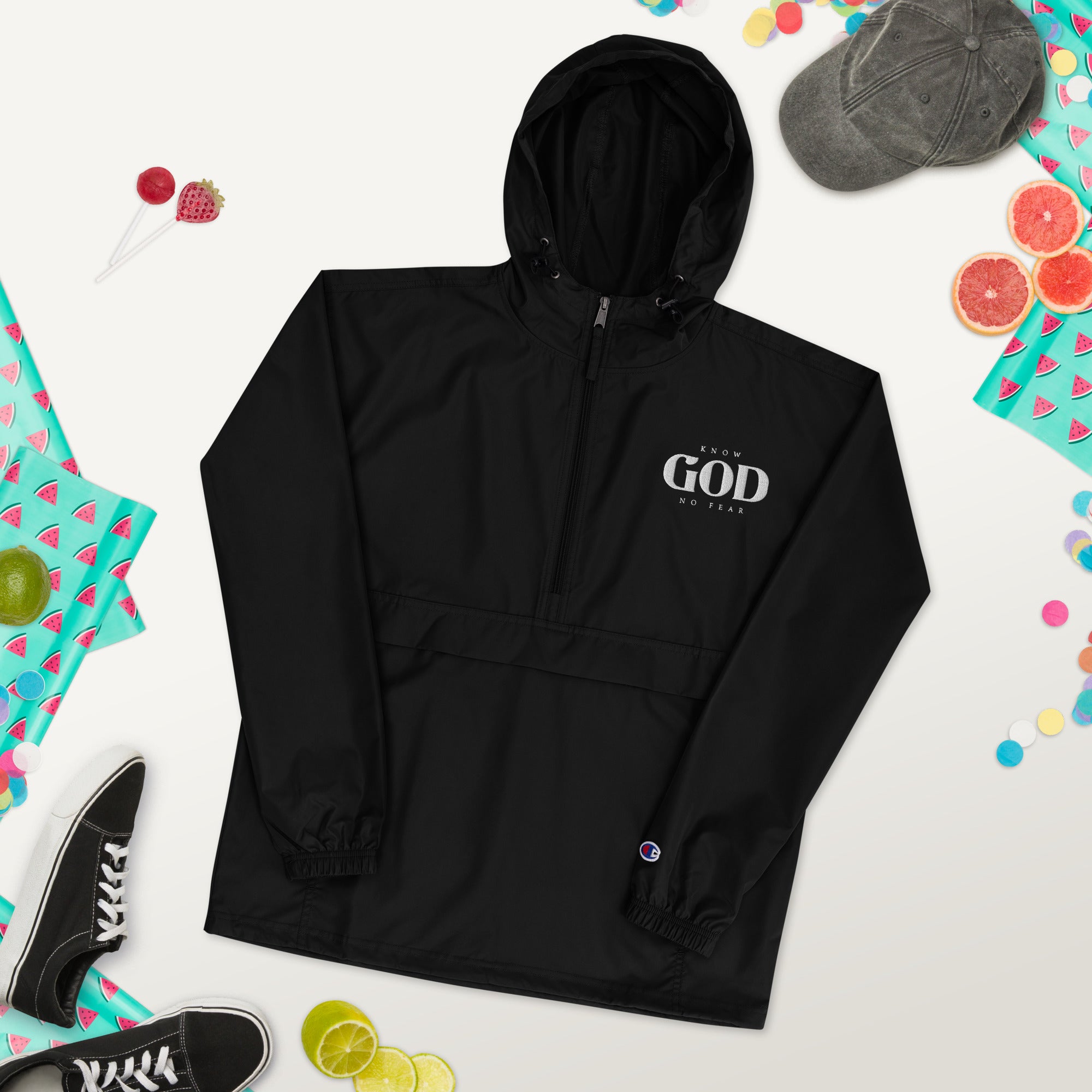 Black Faith-Mark Champion Packable Jacket with "Know God, No Fear" embroidery, surrounded by casual summer accessories like shoes, hat, and fruit, reflecting faith and style.